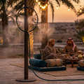 Outdoor standing misting cooling system with brass nozzle ring set up beside a majlis-style outdoor seating area at dusk